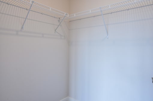 a corner of a room with white walls and a white wire shelving unit