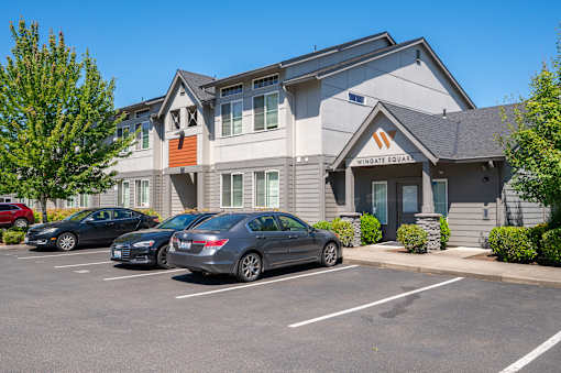 A parking lot in front of a building with cars parked.