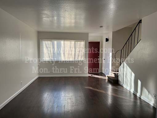 A spacious room with wooden floors and a staircase.