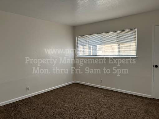 A room with a window covered by blinds and a door on the right side.