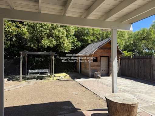 A small wooden building with a sign that reads "Property Management" is surrounded by a wooden fence and a bench under a canopy.