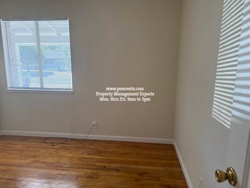 A room with a wooden floor and a window with blinds.