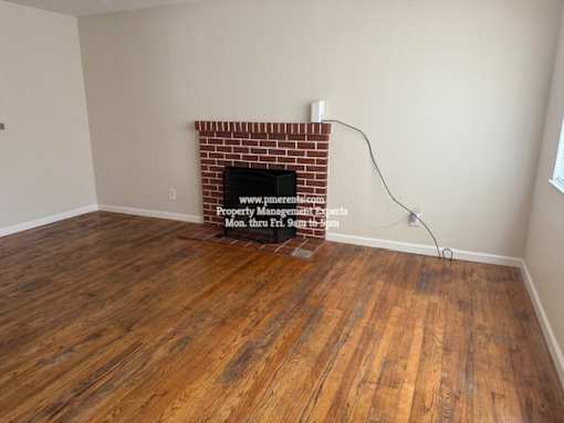 A room with a brick fireplace and wooden floors.