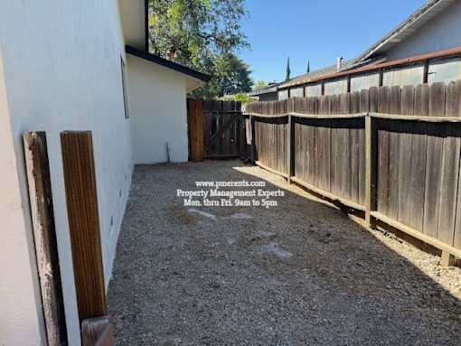 A backyard with a wooden fence and a gravel ground.