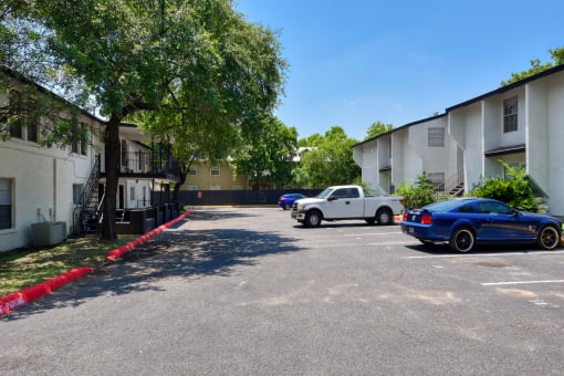 a parking lot between two apartment buildings with cars parked in front