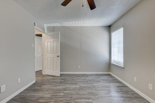an empty living room with a white door and a ceiling fan