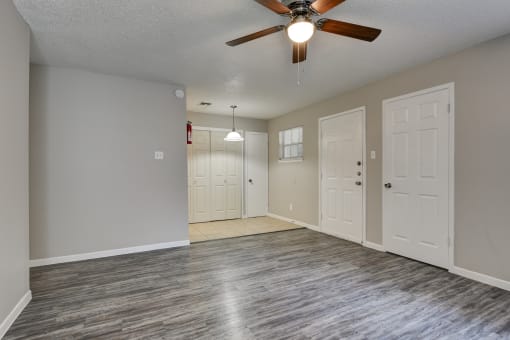 an empty living room with a ceiling fan and white doors
