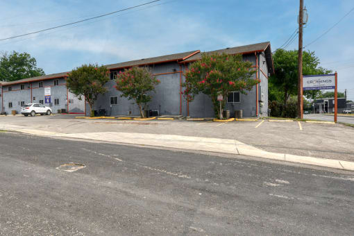 a large white building with trees in front of it on a street at The Crossings at Montrose Apartments, Texas, 78223