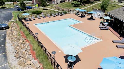 A large outdoor swimming pool surrounded by a fence and lounge chairs.