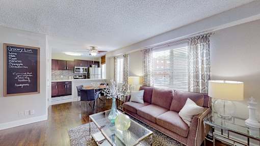 A living room with a couch, coffee table, and a grocery list on the wall.