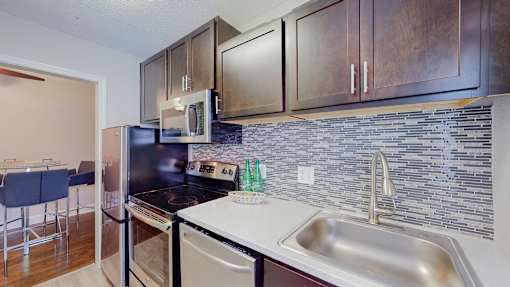 A kitchen with a black fridge, white countertop, and wooden cabinets.