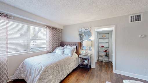 A bedroom with a bed, nightstand, and window with blinds.