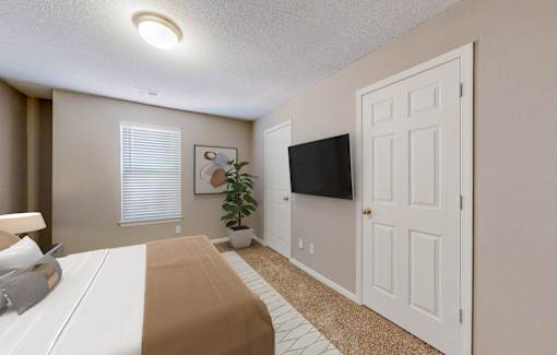 A bedroom with a bed, a plant, a television, and a door.