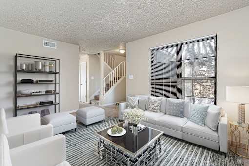 A living room with a white couch, a coffee table, and a staircase in the background.