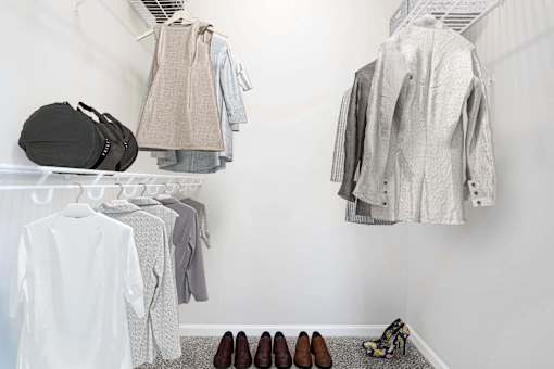 A white closet with clothes and shoes.