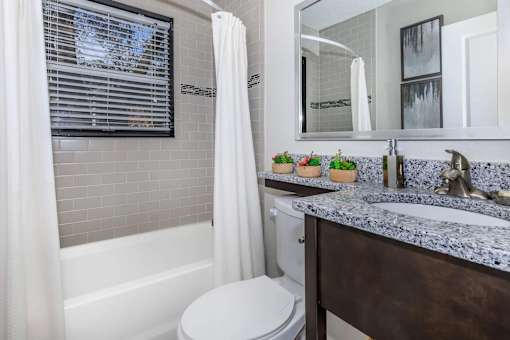 A bathroom with a white toilet, a sink with a marble countertop, and a bathtub with a white shower curtain.