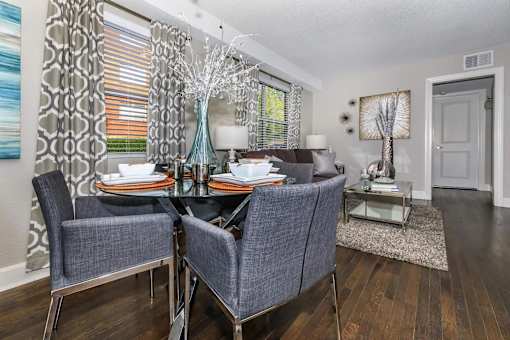 A dining room with a glass table and grey chairs.