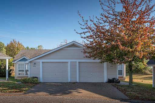 A house with a white garage door is in front of a tree with red leaves.