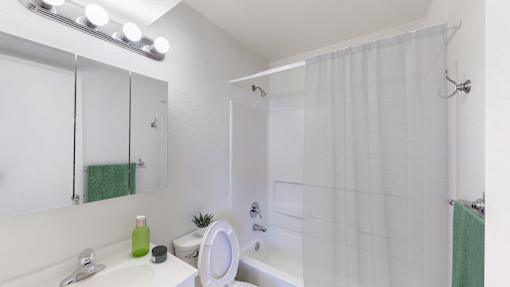 A white bathroom with a green towel and a green bottle on the sink.