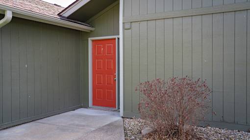 A red door is on the left side of a grey building.