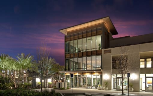 A modern building with a glass facade and a wooden roof is illuminated at night at Circa 37 Apartments, San Diego, CA