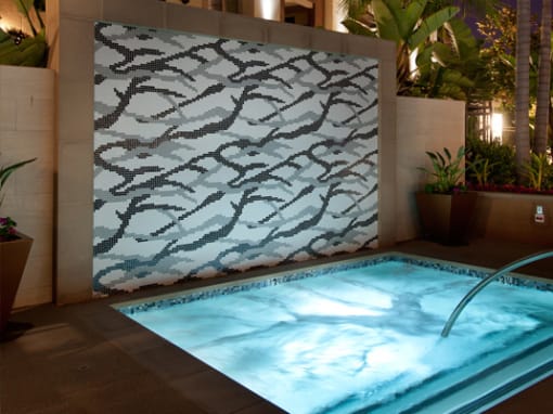 A pool with a light blue tinted water and a wall with a tree pattern at Circa 37 Apartments, San Diego, CA, 92108