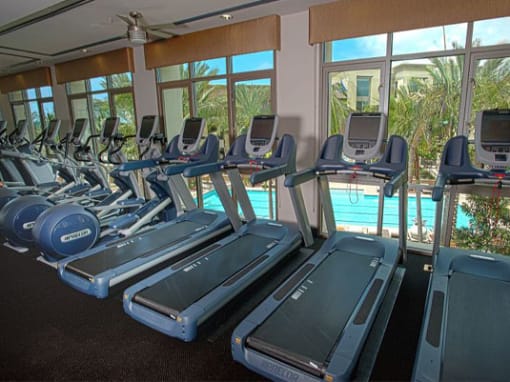 A row of treadmills in a gym with a fan and windows in the background at Circa 37 Apartments, California, 92108