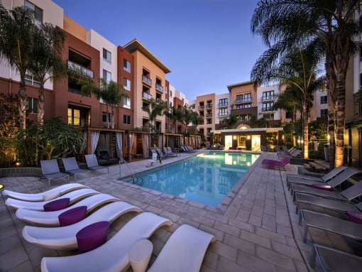 A pool surrounded by lounge chairs and palm trees at West Park Apartments, California, 92108