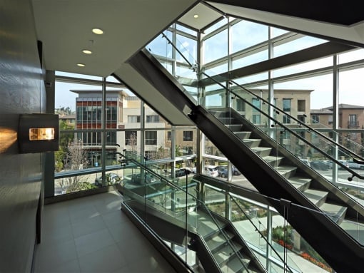 A staircase with glass railings leads to a brightly lit atrium at West Park Apartments, San Diego, California