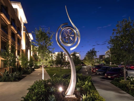 A large, illuminated sculpture in the shape of a spiral is the focal point of a well-lit garden area.  at West Park Apartments, San Diego, CA