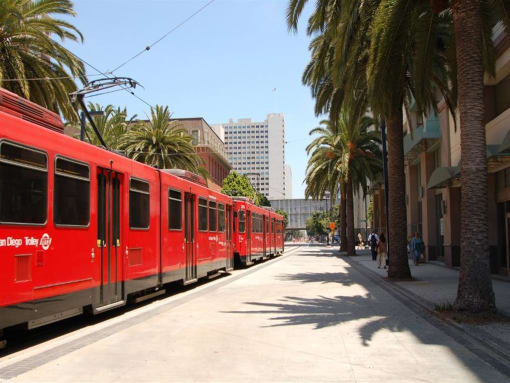 A red trolley car is on a track with palm trees on the side at West Park Apartments, San Diego, 92108
