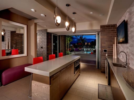 A modern kitchen with a long island and red chairs at West Park Apartments, San Diego