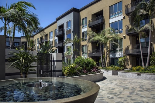 A fountain in the middle of a courtyard surrounded by buildings and palm trees at Purl Apartments, San Diego, CA, 92108
