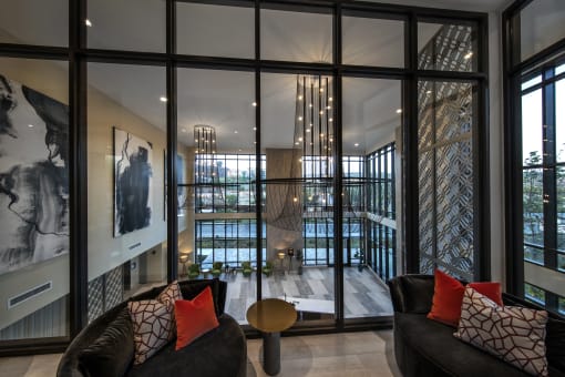 A black couch with red pillows sits in front of a large window at Purl Apartments, California