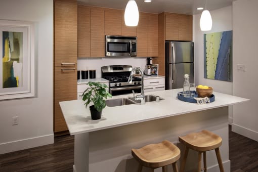 A kitchen with a white countertop and wooden stools at West Park Apartments, San Diego, California