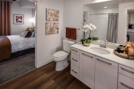 A bathroom with a toilet, sink, and bedroom area at West Park Apartments, San Diego
