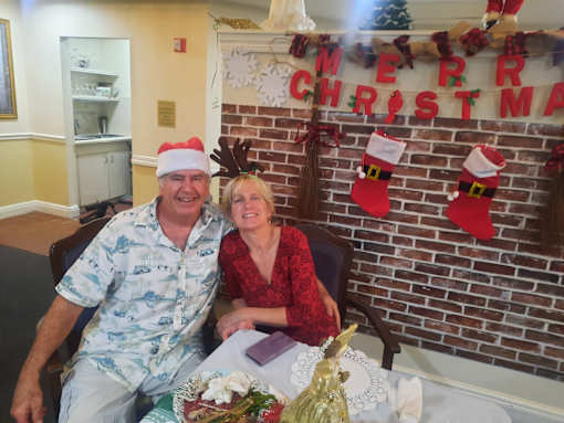 A man and woman sitting in front of a Merry Christmas sign  at Savannah Grand of Sarasota, Sarasota, 34238.