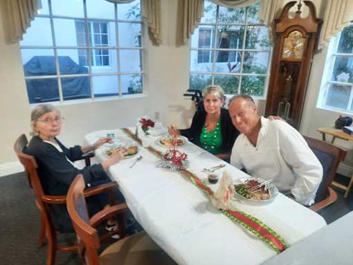 Three people are sitting at a table with a white tablecloth and a long centerpiece. at Savannah Grand of Sarasota, Sarasota, 34238.