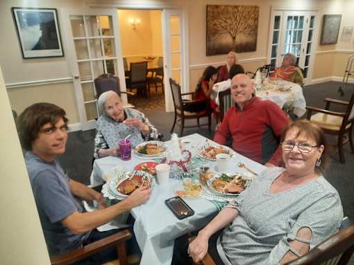 A group of people are sitting around a table with plates of food in front of them  at Savannah Grand of Sarasota, Sarasota, FL.