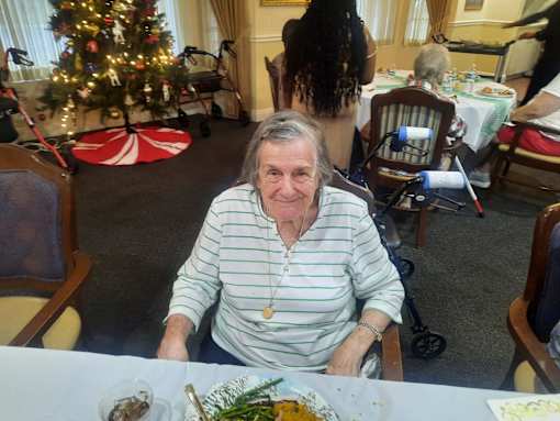 A woman in a striped shirt sits at a table with a Christmas tree in the background  at Savannah Grand of Sarasota, Sarasota, 34238.