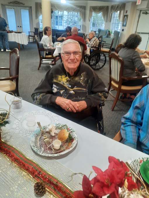 A man in a wheelchair sits at a table with a plate of food in front of him  at Savannah Grand of Sarasota, Sarasota, 34238.