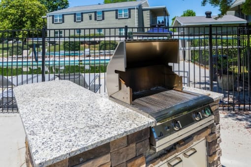 an outdoor grill with a stone table in front of a pool
