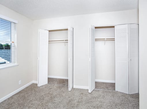an empty bedroom with three closet doors and a window