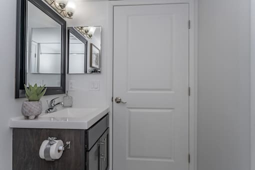 A bathroom with a white door and a mirror above a sink.