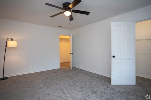 an empty living room with a ceiling fan and a white door