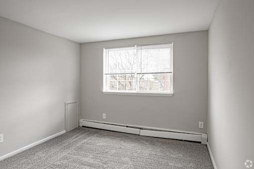 A room with a window and a carpeted floor.