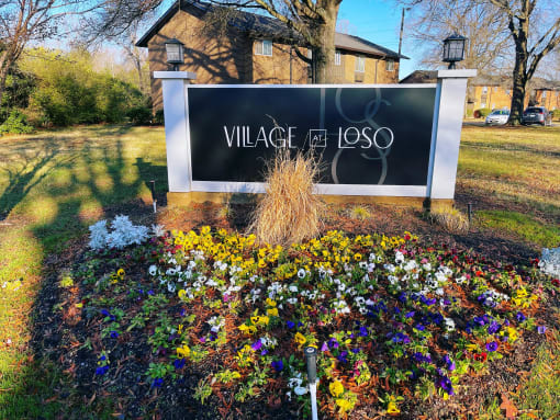 a sign for village of lasso in front of a garden of flowers