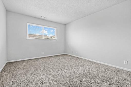 A room with a carpeted floor and a window showing a building outside.