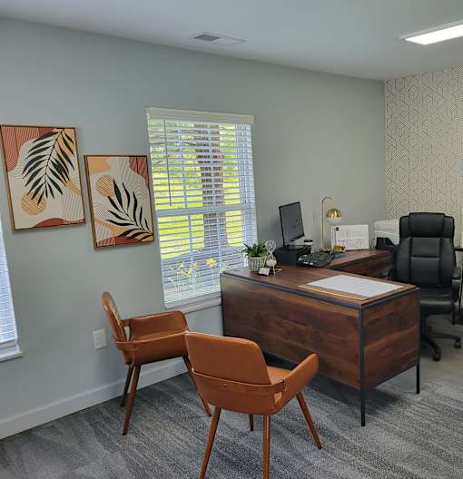 A room with a desk, chair and two paintings on the wall.