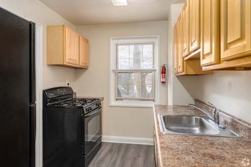 A kitchen with a black refrigerator, black stove, and wooden cabinets.